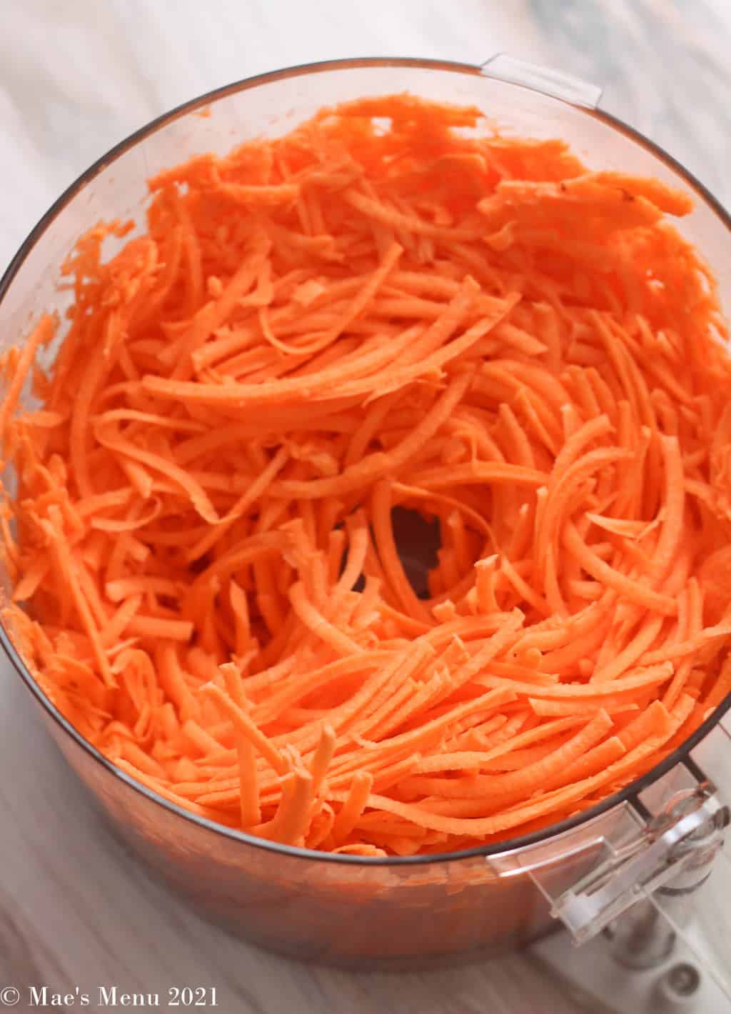 A food processor bowl of shredded sweet potatoes