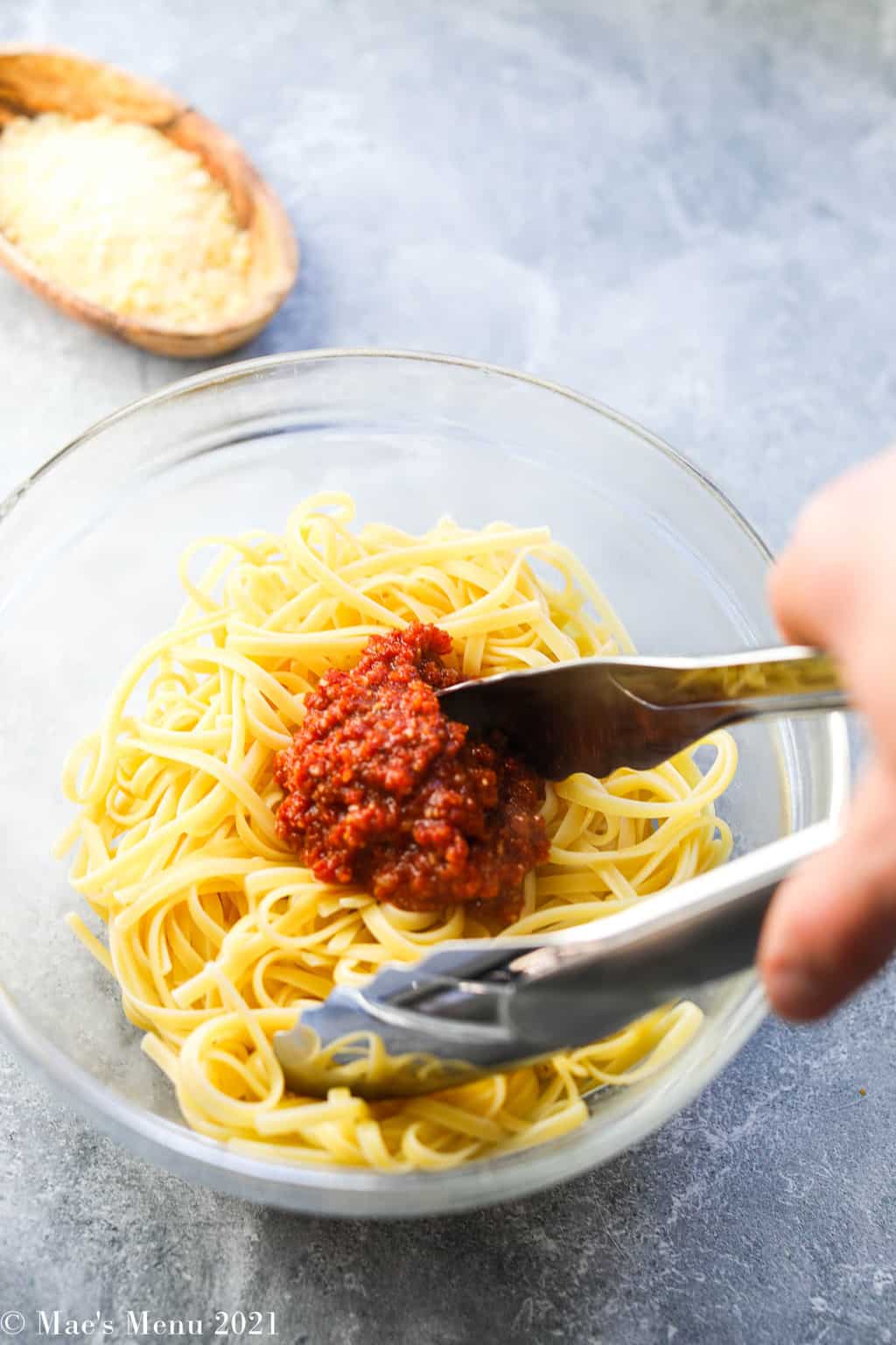 Tossing pasta with the tomato pesto in a glass mixing bowl