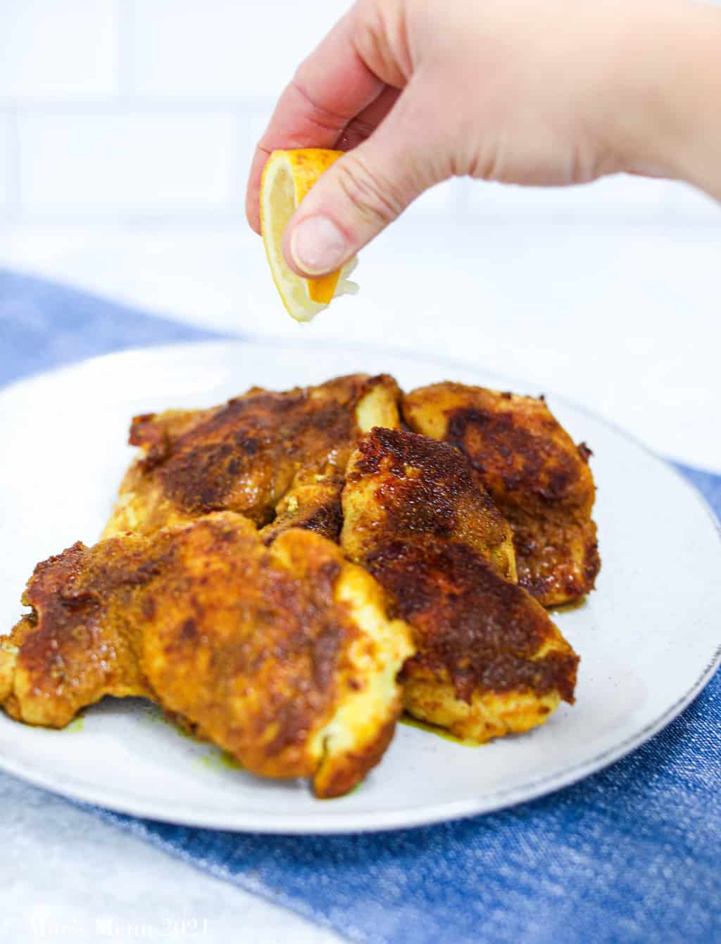A small plate of turmeric rubbed chicken with a hand squeezing lemon juice over it
