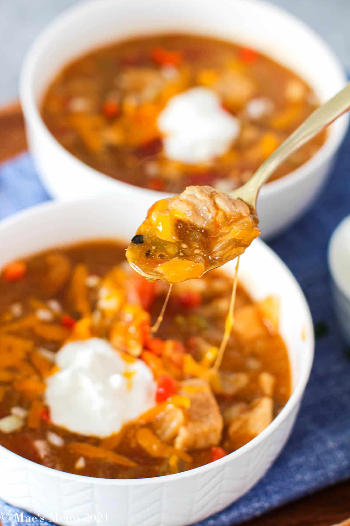 A large spoonful of pork green chili with cheese strings dripping from the spoon