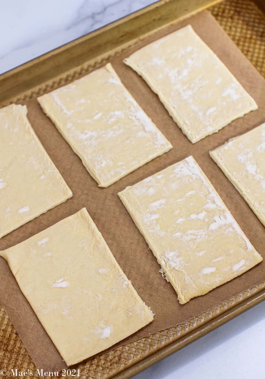 A parchment paper lined baking sheet with rectangles of puff pastry on it 