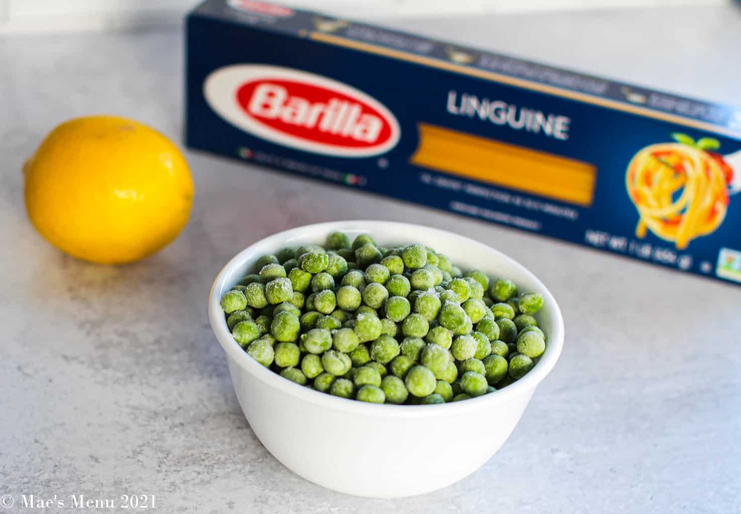 a small white dish of frozen green peas, a whole lemon, and a package of barilla linguine