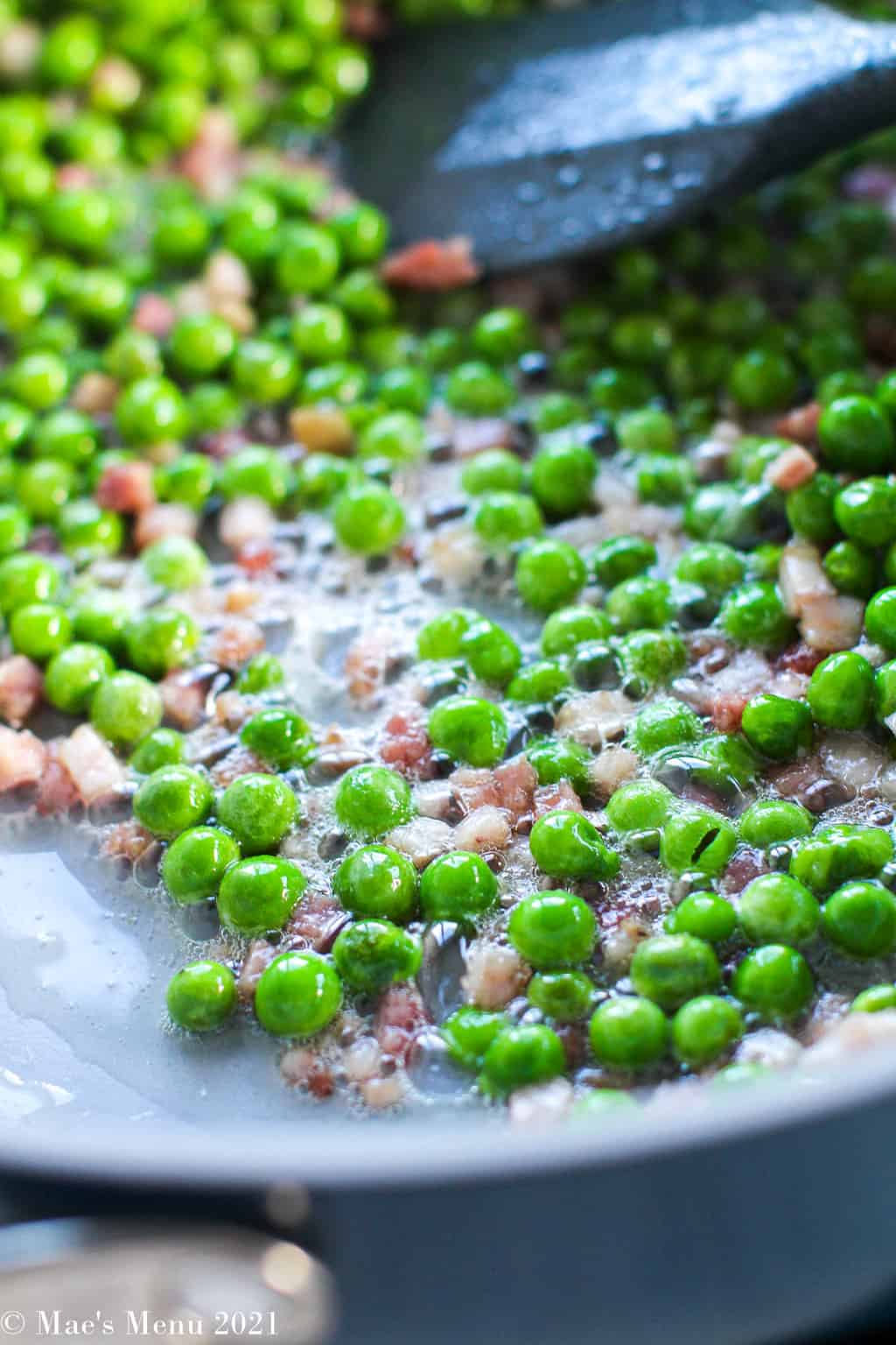 an up-close shot of pancetta and peas cooking in a non-stick pan