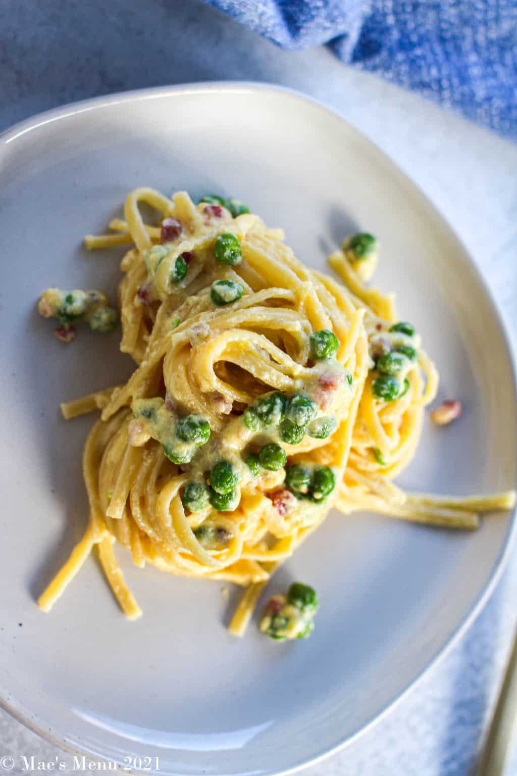 An angled overhead shot of a white plate flute of creamy lemon ricotta pasta with peas