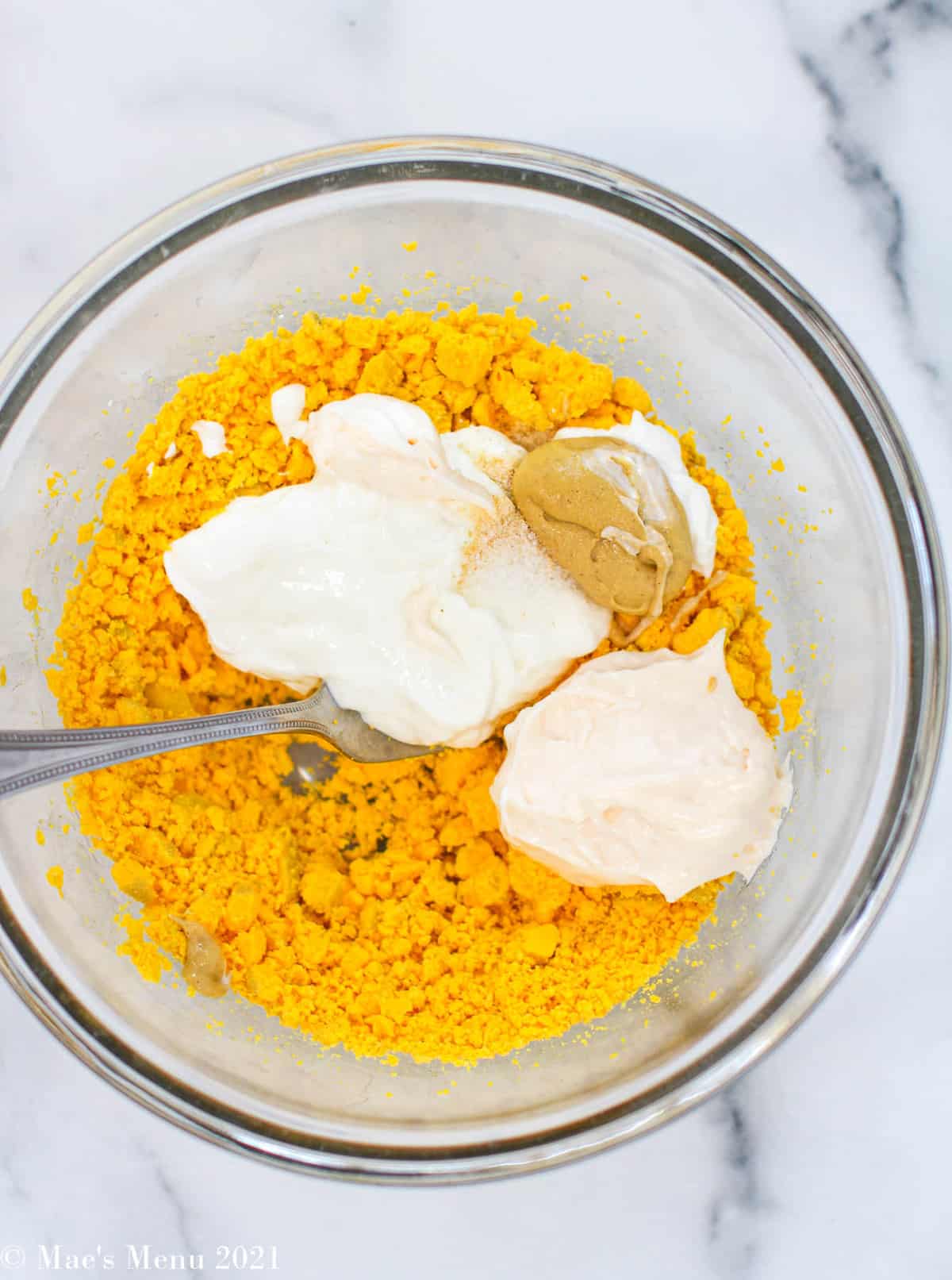 Crumbled egg yolk in a glass bowl with greek yogurt, mayonnaise, dijon mustard, onion powder, and salt 