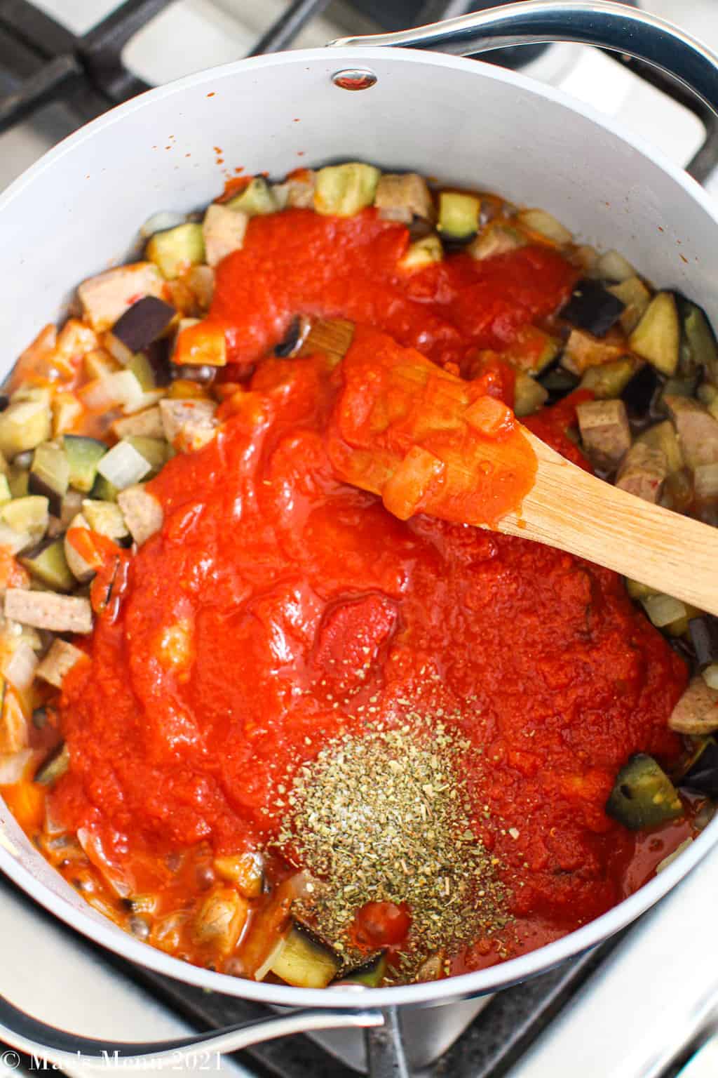 Stirring the crushed tomatoes and seasonings into the sausage and eggplant 