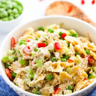 A large white bowl of tuna macaroni salad with wooden tongs in the background