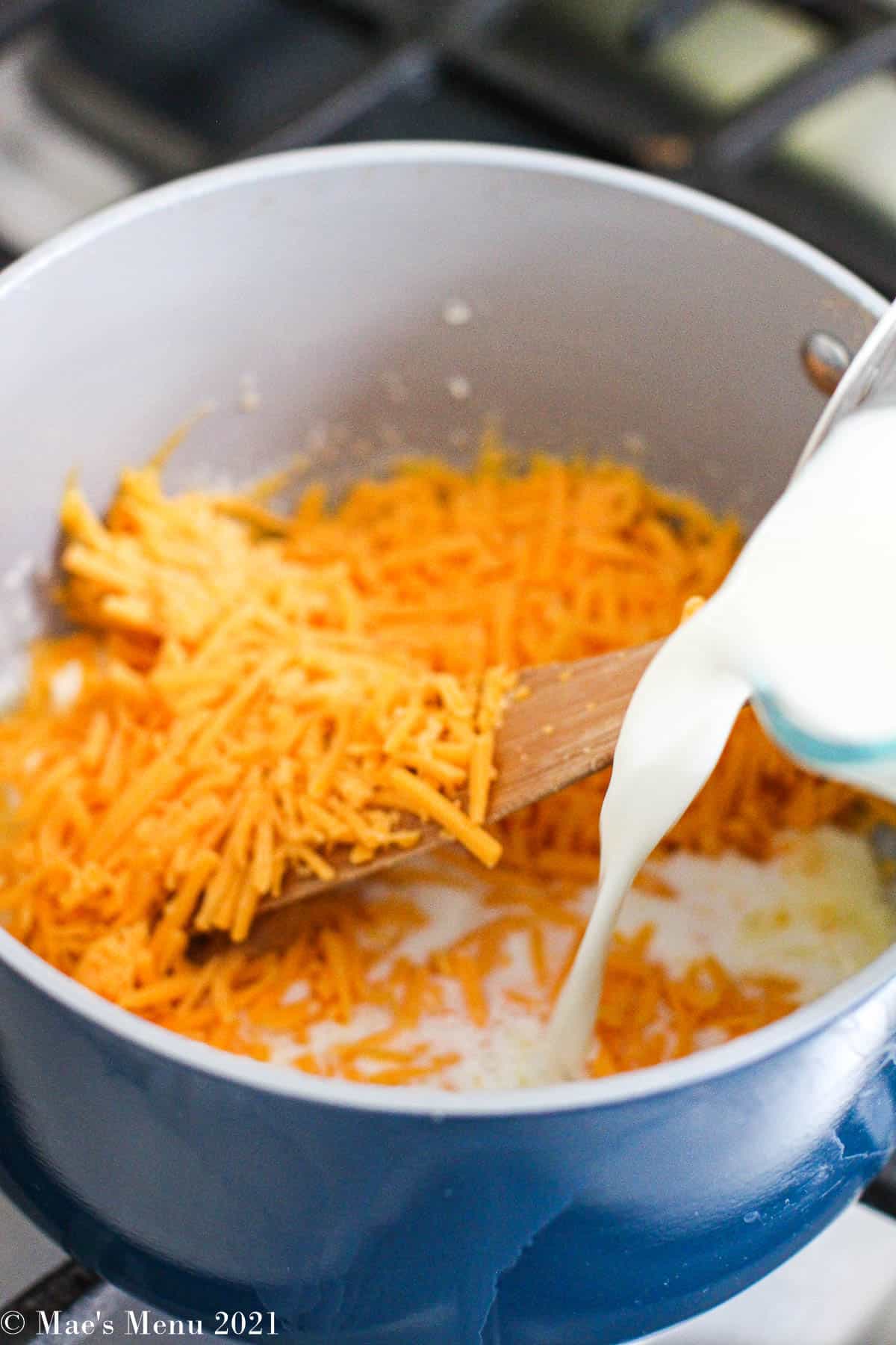 Shredded sharp cheddar cheese, and butter with milk pouring into the pan