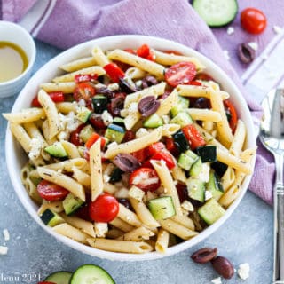 an overhead shot of a bowl of pasta salad surrounded by veggies and a spoon