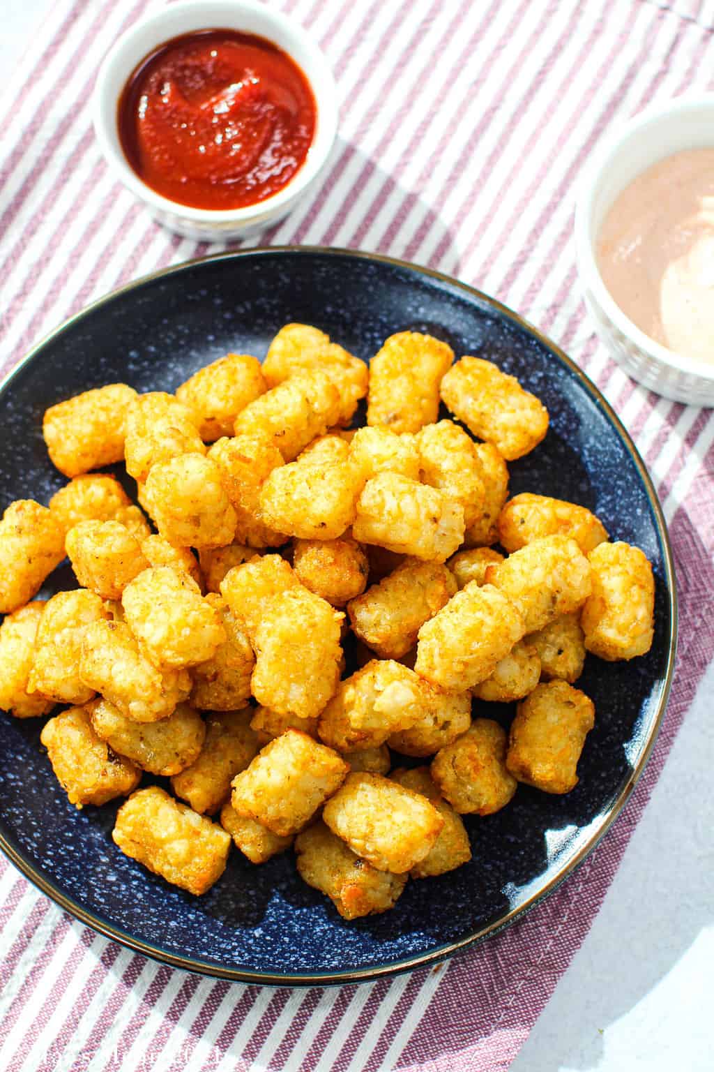 A plate of air fryer tater tots with a cup of ketchup and srircha mayo