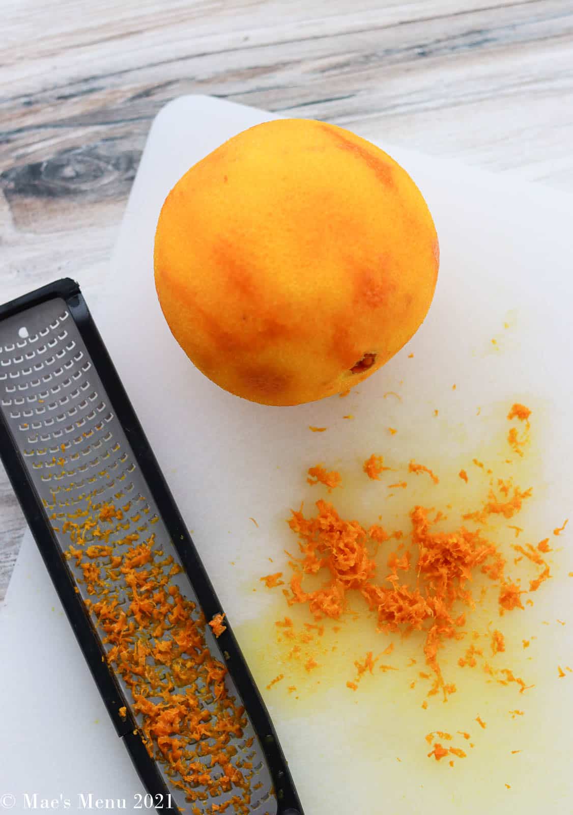 A zested orange with a microplane zester and orange zest on a cutting board