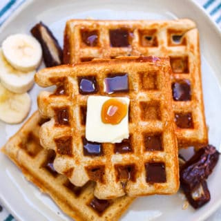 An overhead shot of a whole wheat waffle with butter, maple syrup, bananas, and dates