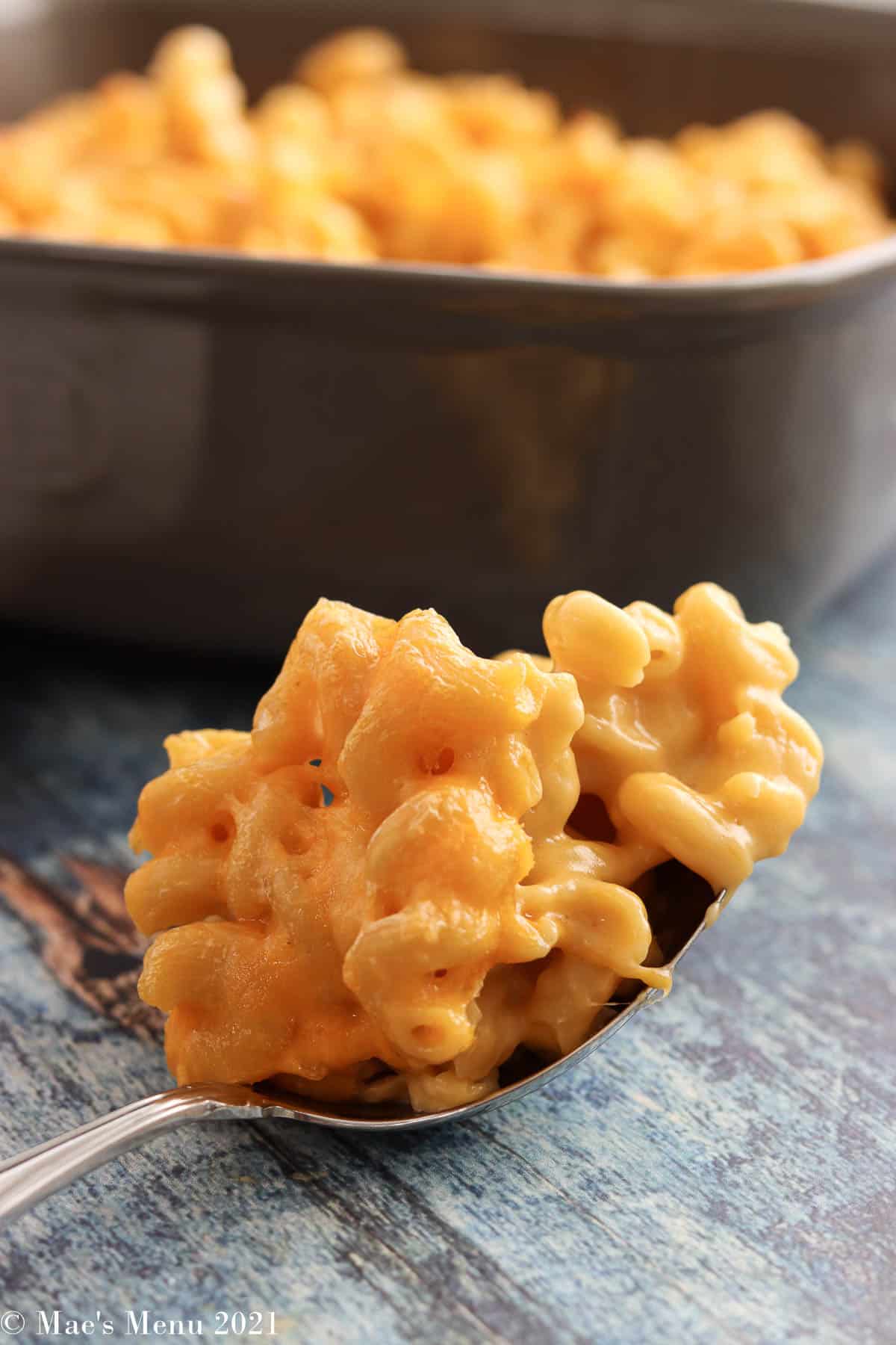 A large scoop of healthy mac and cheese in front of a baking dish of the recipe