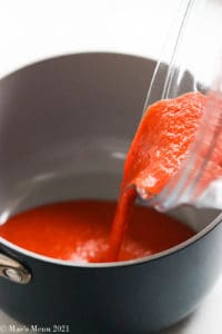 Pouring marinara sauce into a saucepan to simmer