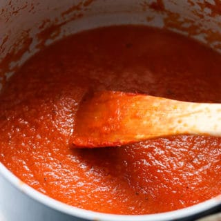A side shot of a saucepan of marinara sauce with a wooden spoon