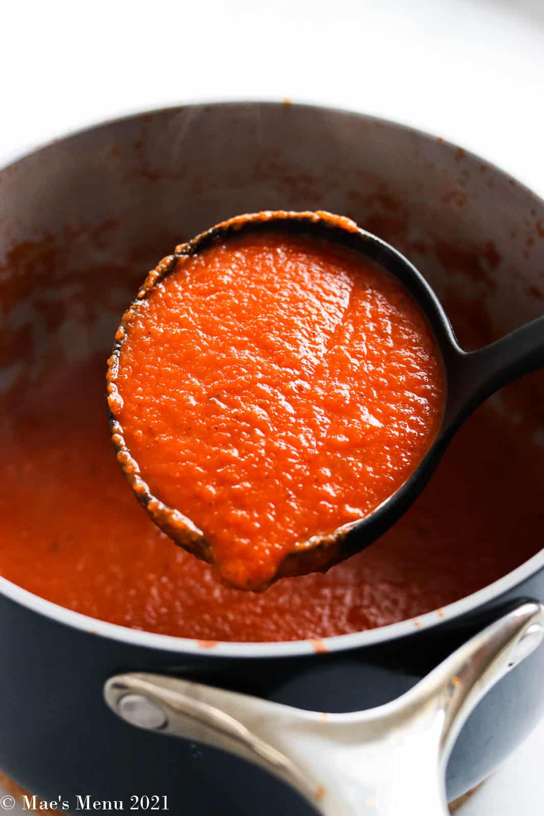A large ladle of marinara sauce over a saucepan