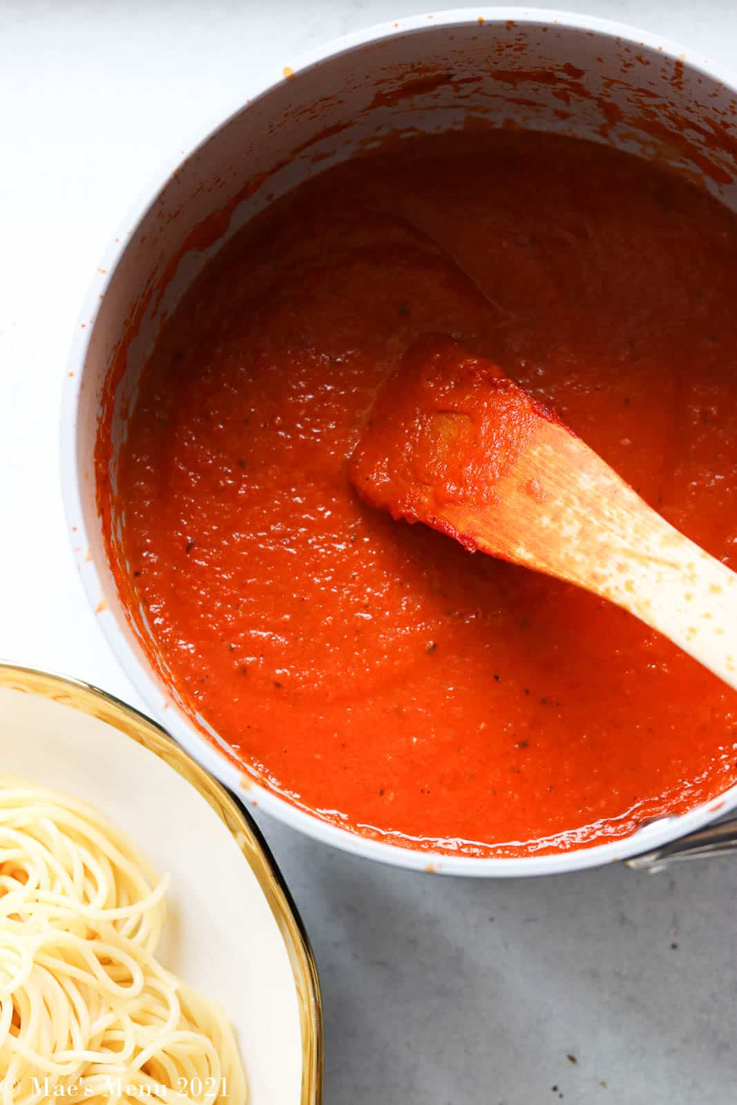 An overhead shot of a saucepan of marinara sauce next to a bowl of pasta