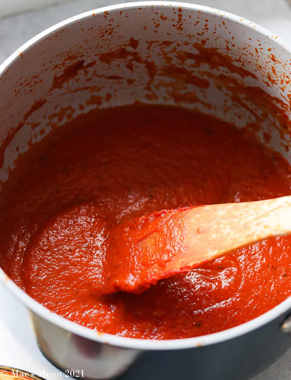 A side shot of a saucepan of marinara sauce with a spatula in it 