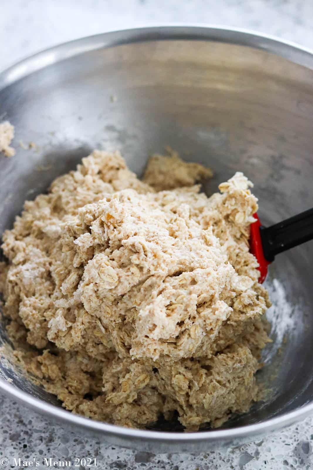 A large mass of oatmeal bread dough in a mixing bowl