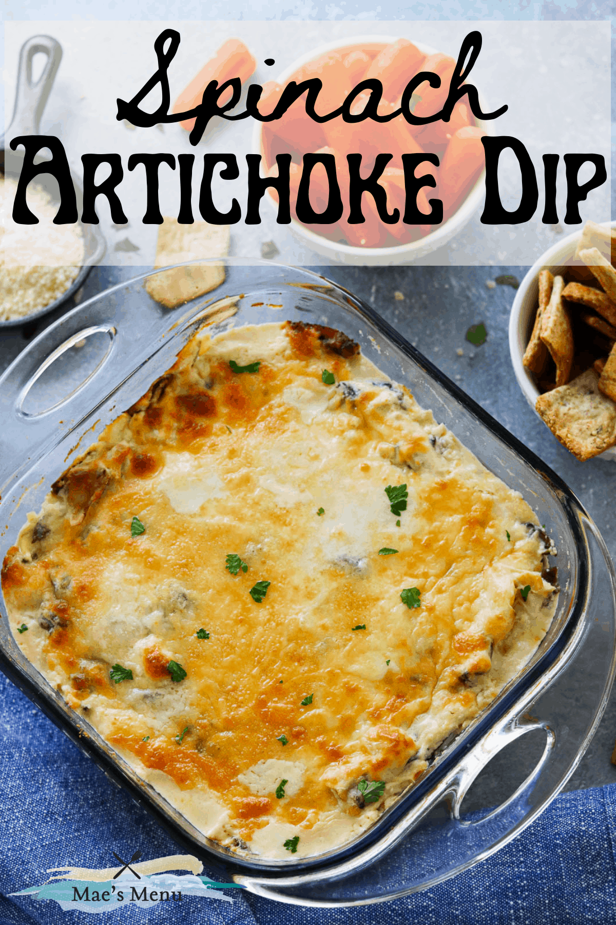A pinterest pin for spinach artichoke dip with an overhead shot of a pan of the dip surrounded by crackers and veggies 