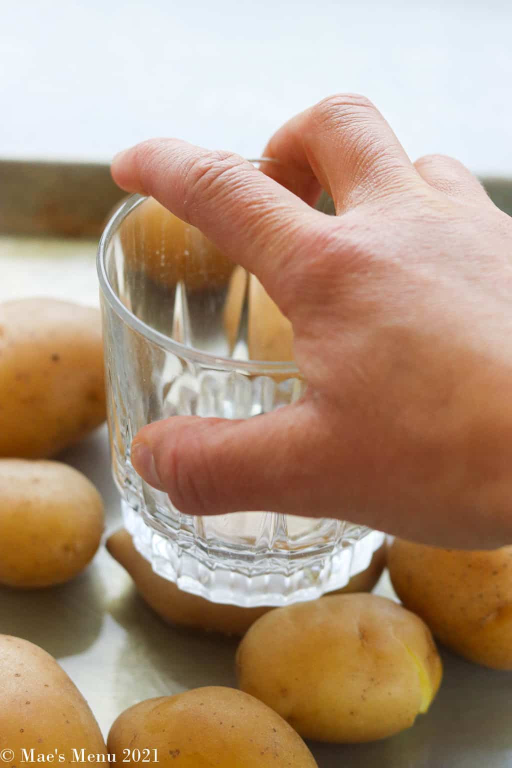 smashing potatoes on a baking sheet with a glass cup