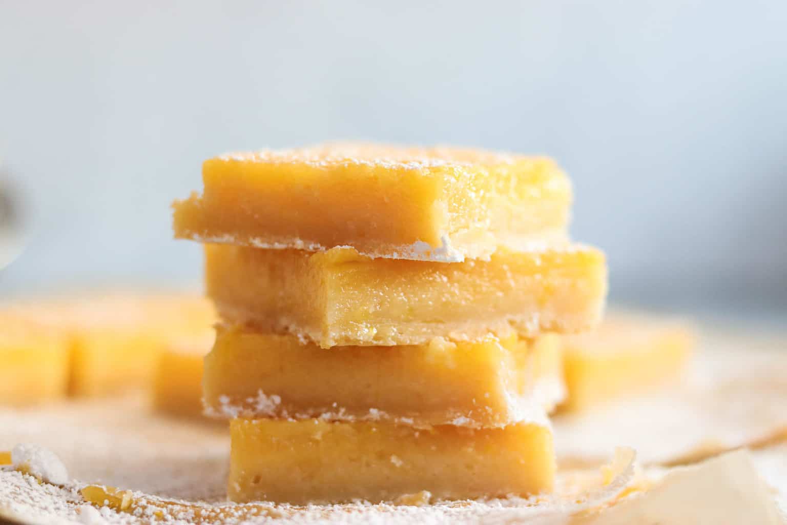 A stack of lemon bars sitting on a piece of parchment paper