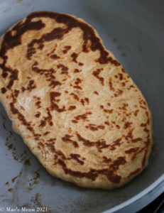 A cooking piece of naan on a skillet