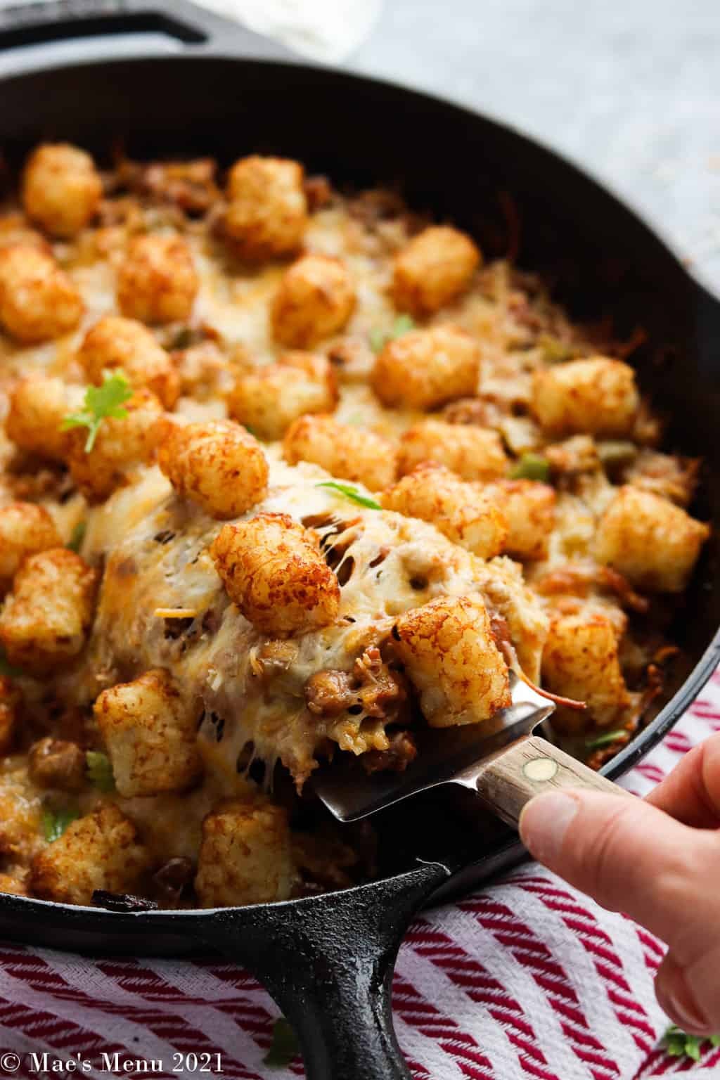 A hand taking a scoop of taco tater tot casserole out of a cast iron skillet 