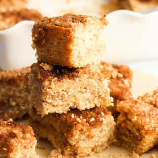 A stack of vegan coffee cake pieces in front of a white pan of the cake