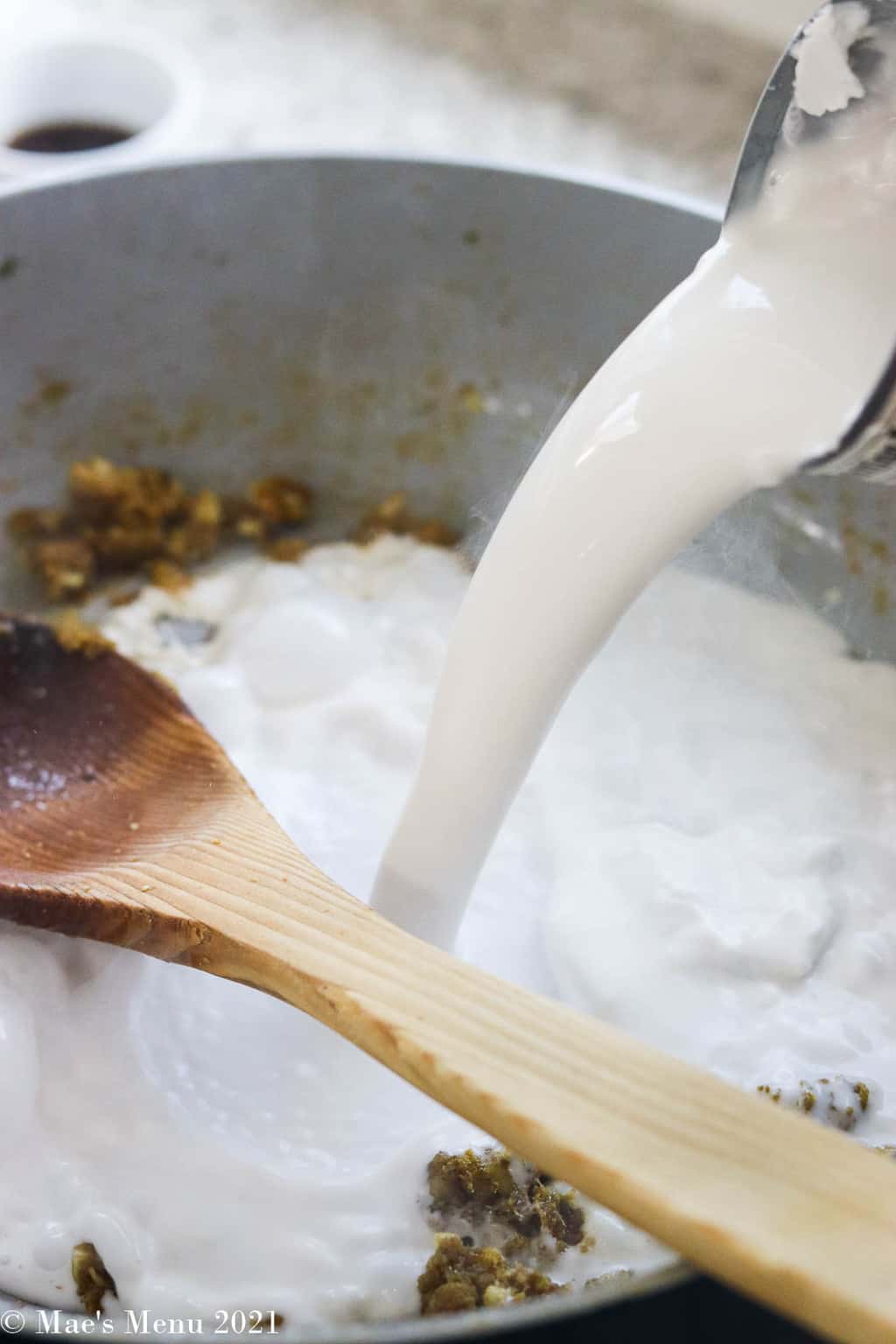 pouring coconut milk into the pan with the curry paste