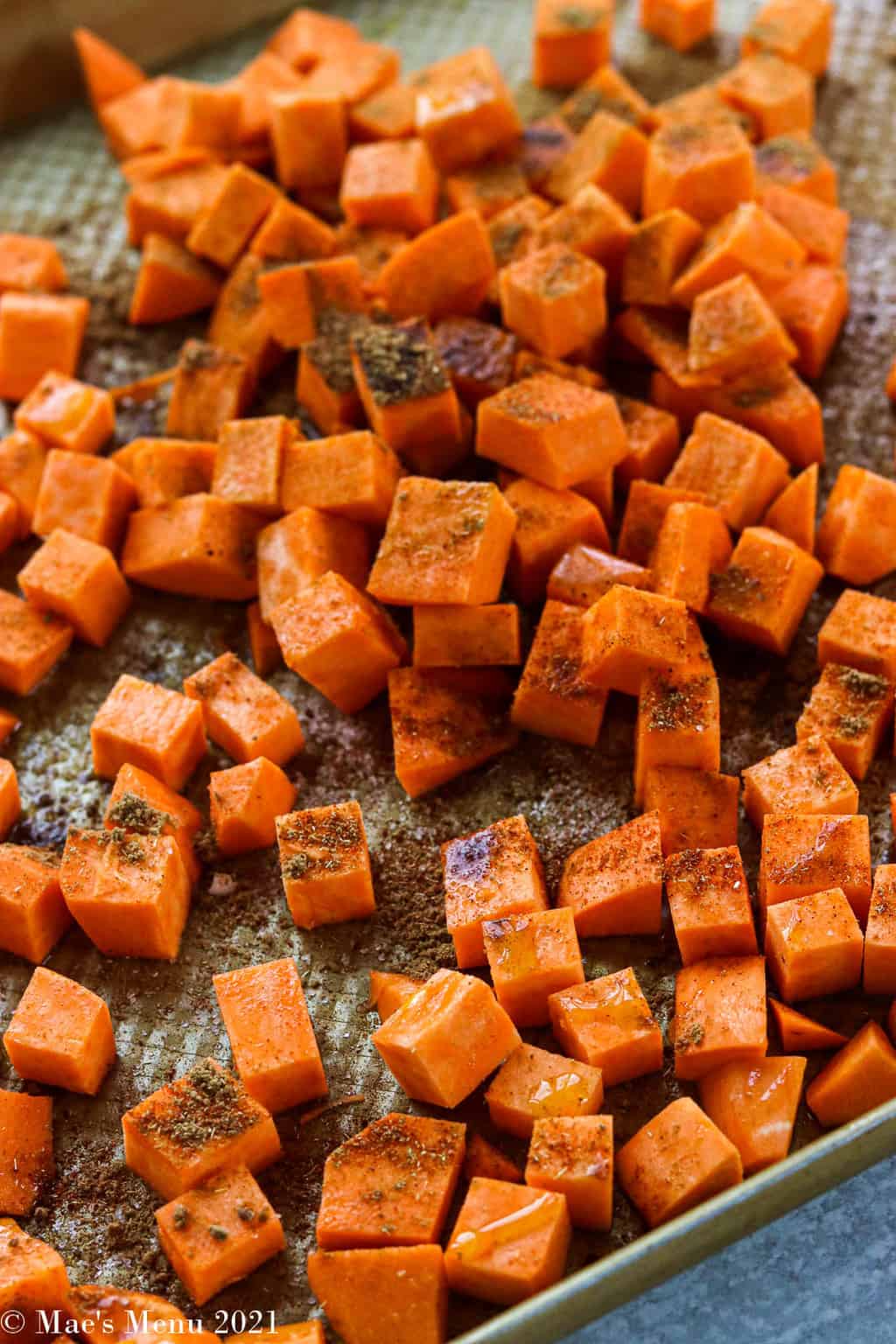 A baking sheet of sweet potatoes drizzled with olive oil and spices