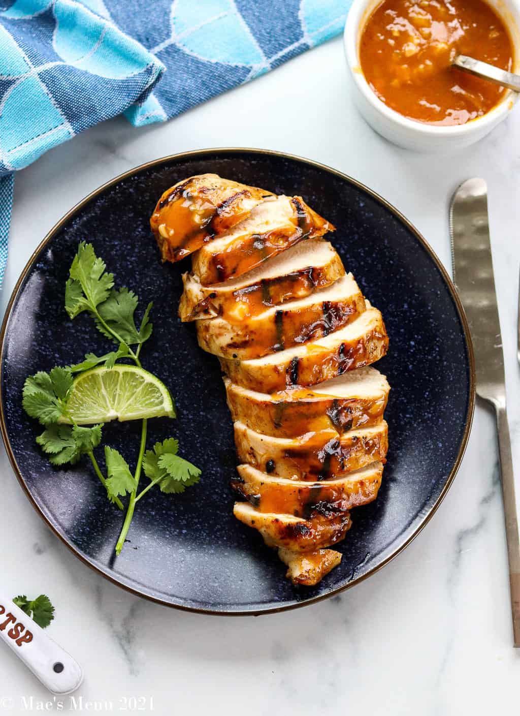 An overhead shot of grilled chicken, sliced on a blue plate with cilantro and lime
