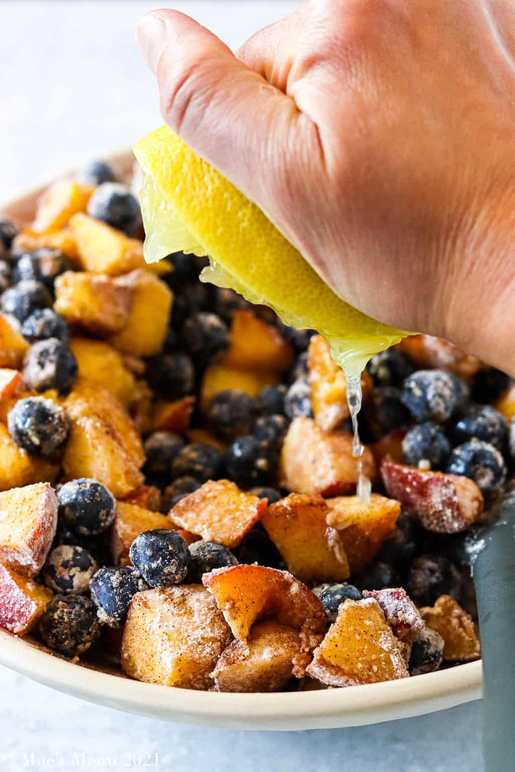 Squeezing lemon juice over a bowl of peaches and blueberries