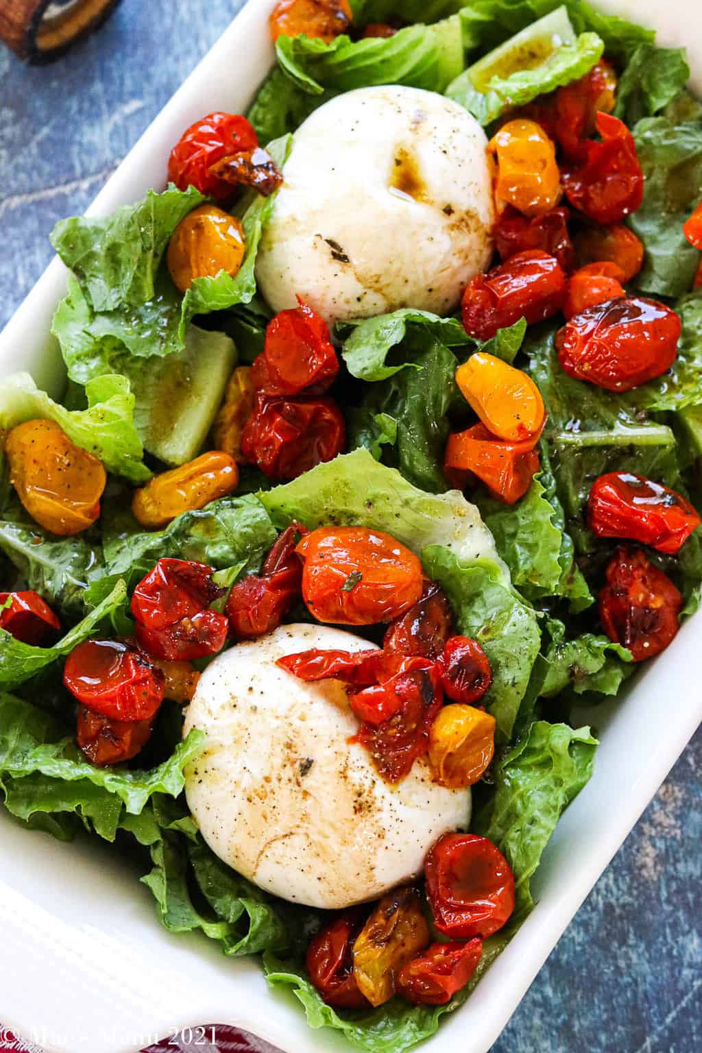 An up-close overhead shot of a platter or burrata salad with roast tomatoes