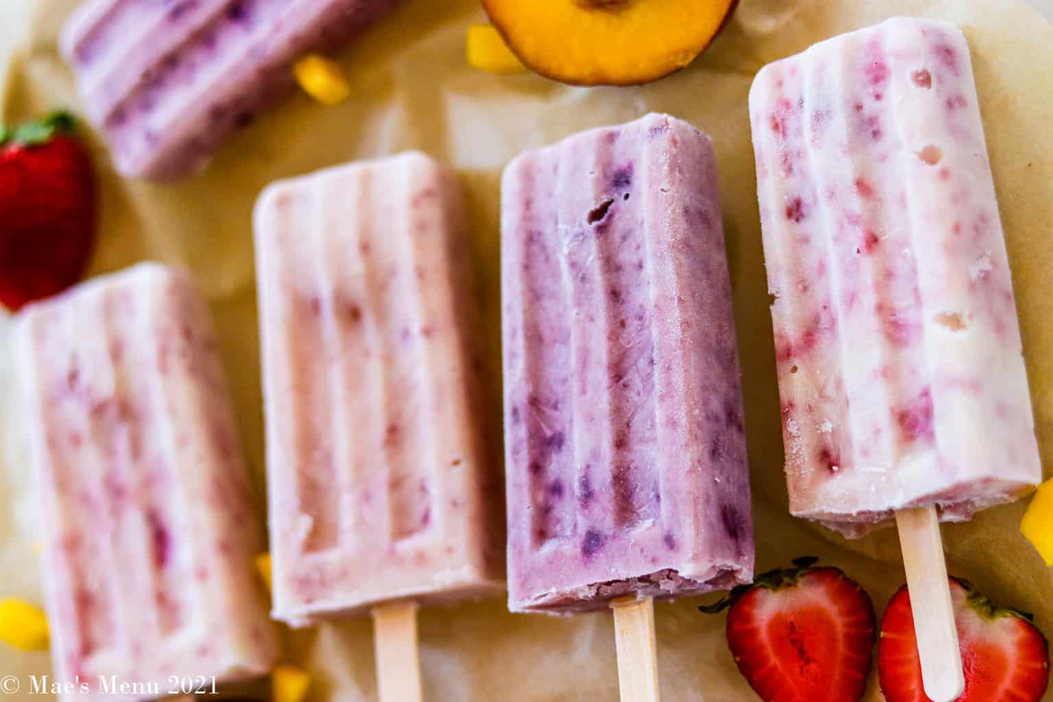 A horizontal shot of 4 yogurt popsicles surrounded by fruit