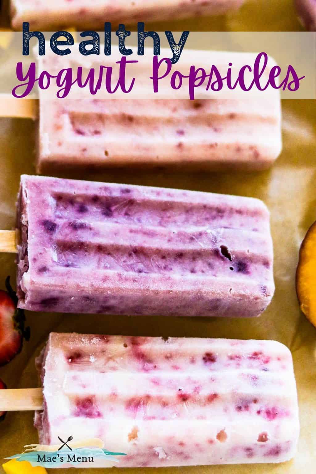 A pinterest pin for healthy yogurt popsicles with an up-close photo of the popsicles on a piece of parchment with fruit