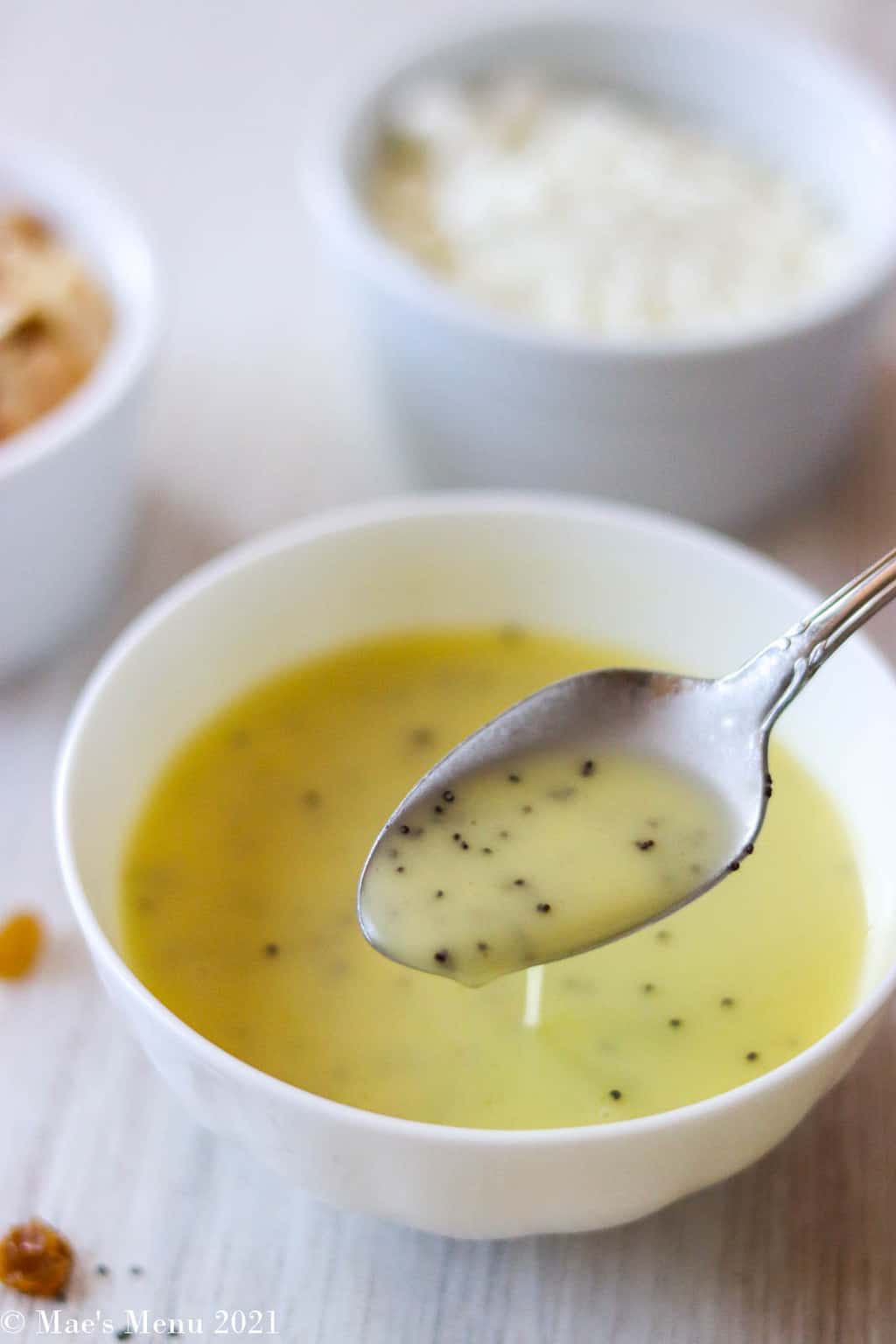 An up-close shot of a bowl of lemon poppy seed dressing with a spoon in it