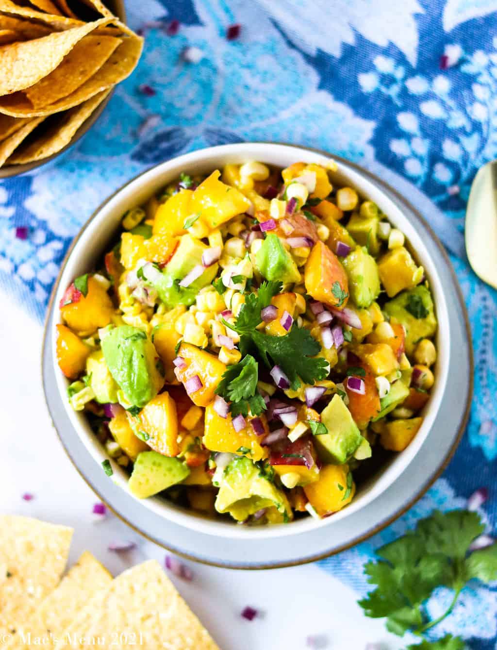 An up-close shot of a bowl of avocado peach salsa with chips around it