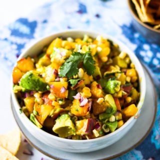 a small serving bowl of avocado peach salsa with chips beside it