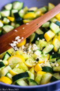 An up-close shot of yellow squash and zucchini with garlic in a saute pan