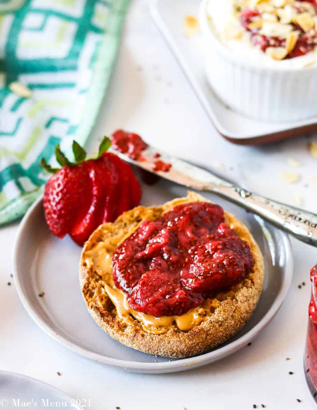 An up-close side shot of an english muffin with peanut butter and strawberry chia jam 