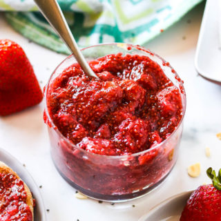 A small dish of strawberry chia jam surrounded by toast and strawberries