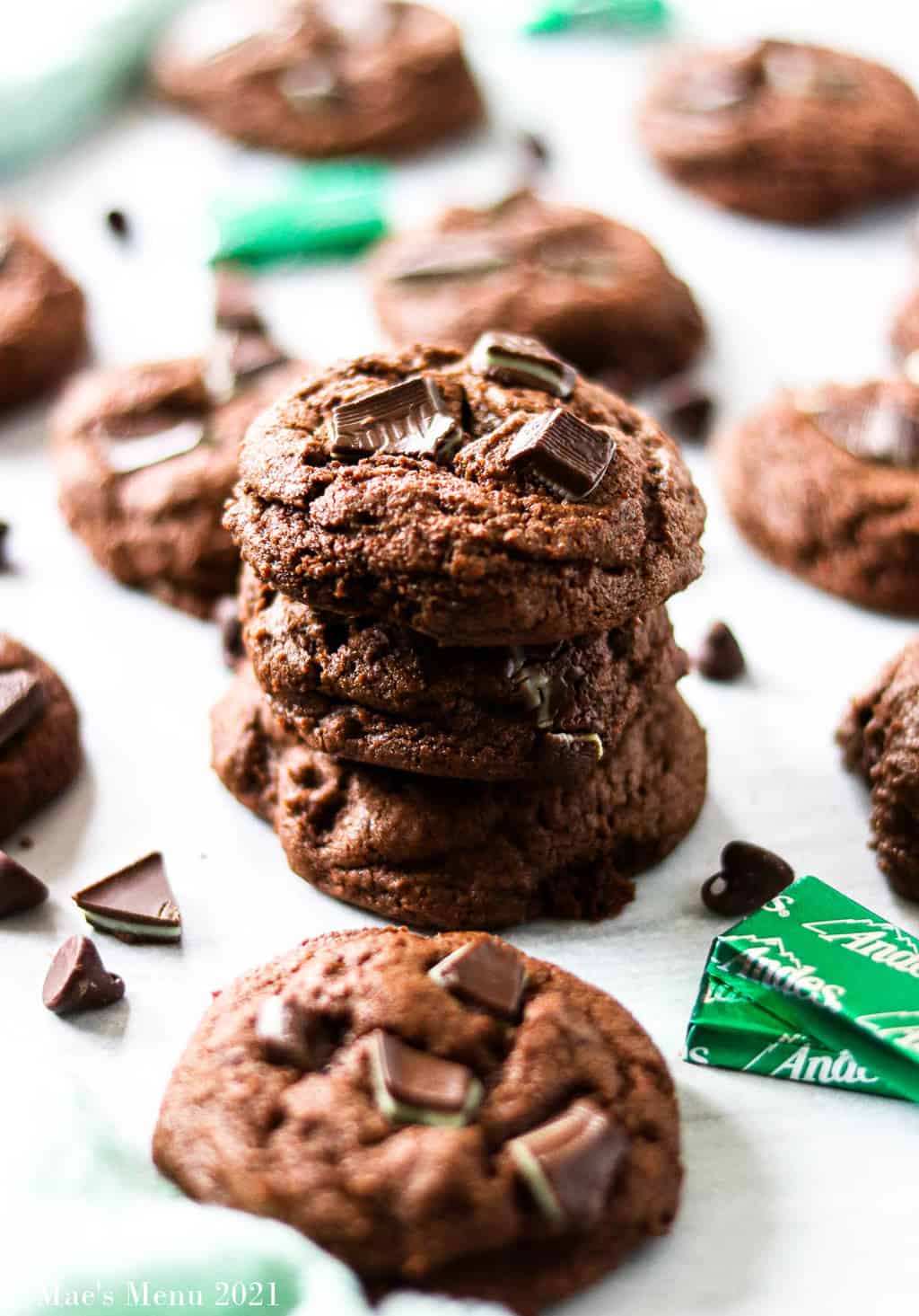A stack of mint chocolate chip cookies with chocoalte chips, mints, and a green towel
