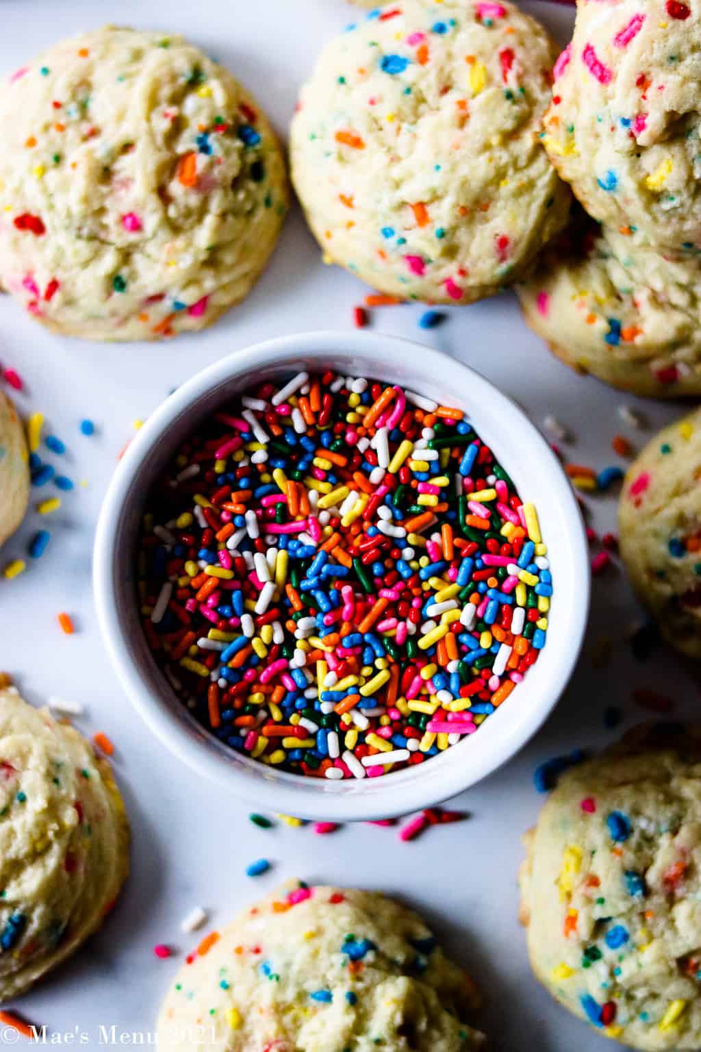 An up-close shot of a dish of rainbow sprinkles surrounded by birthday cake cookies