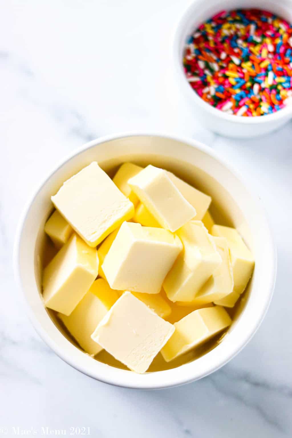 An overhead shot of a dish of cubed butter with a small dish of sprinkles in the background