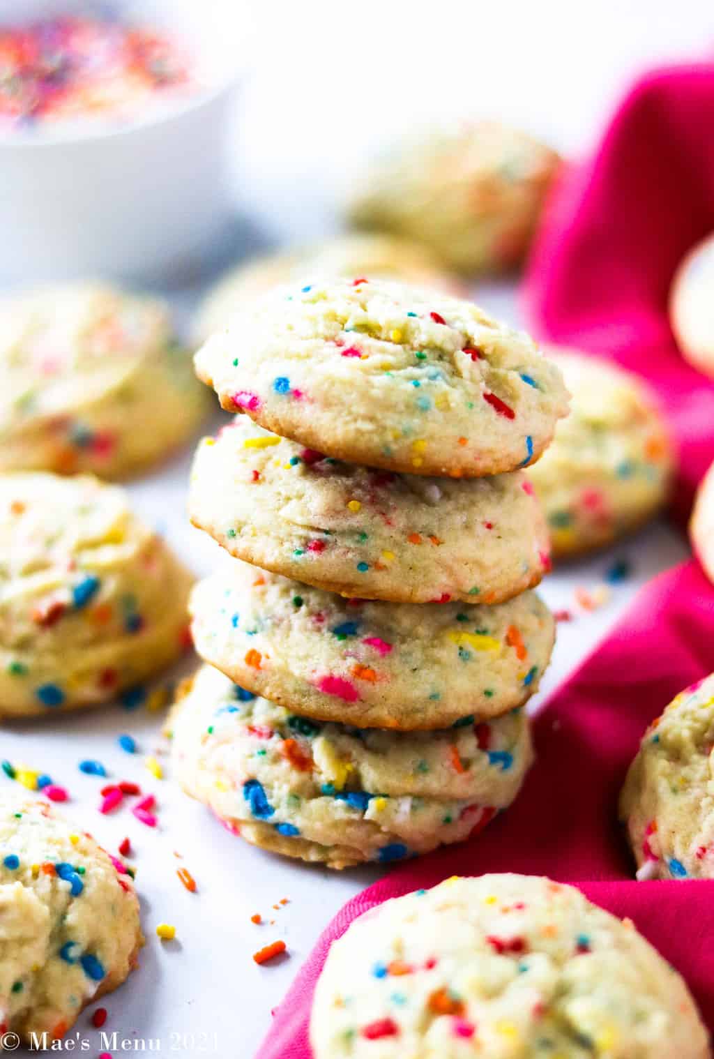 A stack of funfetti cookies on the counter with sprinkles and cookies surrounding them