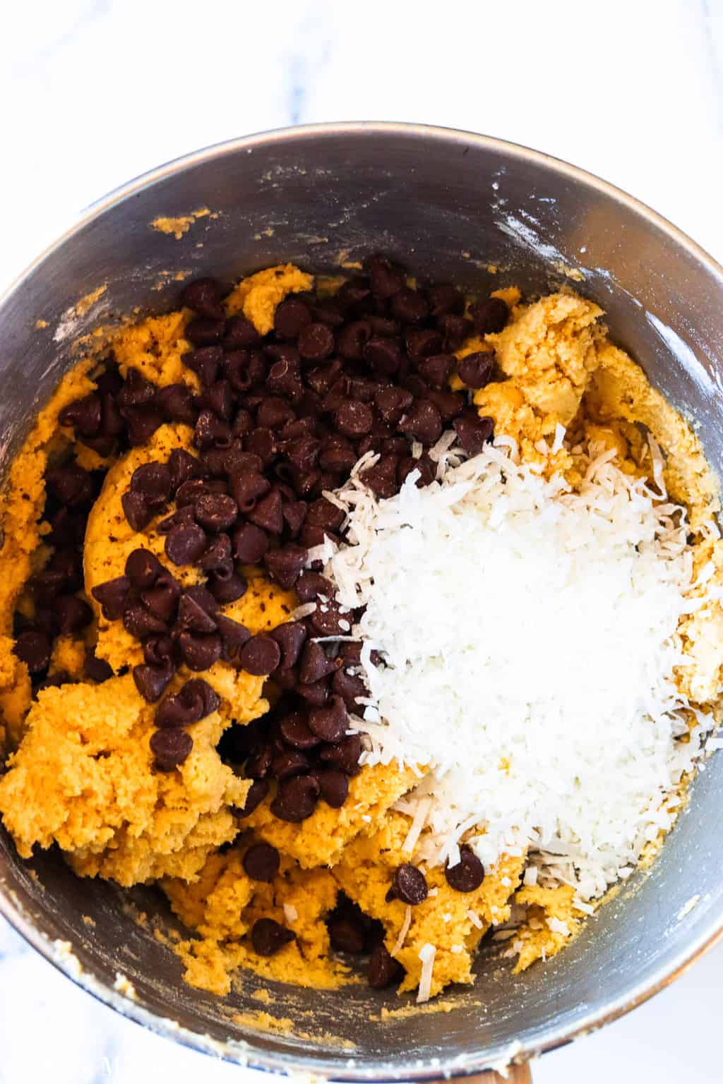 A mixing bowl of cookie dough with chocolate chips and coconut