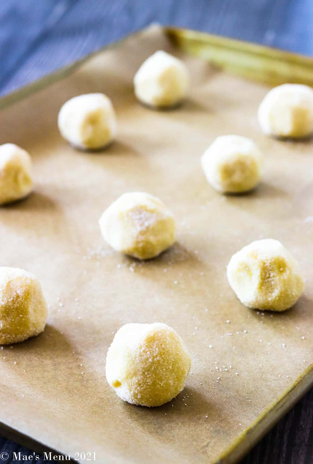 Balls of lemon sugar cookie rolled in granulated sugar on a baking tray with parchment paper