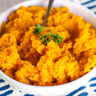 A large white bowl of mashed butternut squash with a small spring of parsley on top