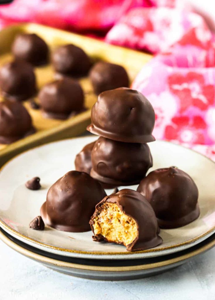 A stack of peanut butter bon bons on a small stack of plates. One bon bon has a bite taken out of it